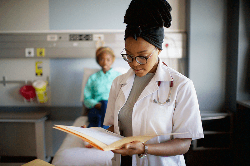 A female doctor holding a patient's file looking down reading - stock photo
A female African doctor holding a patient's file with the patient out of focus sitting on a hospital bed behind Cape Town South Africa